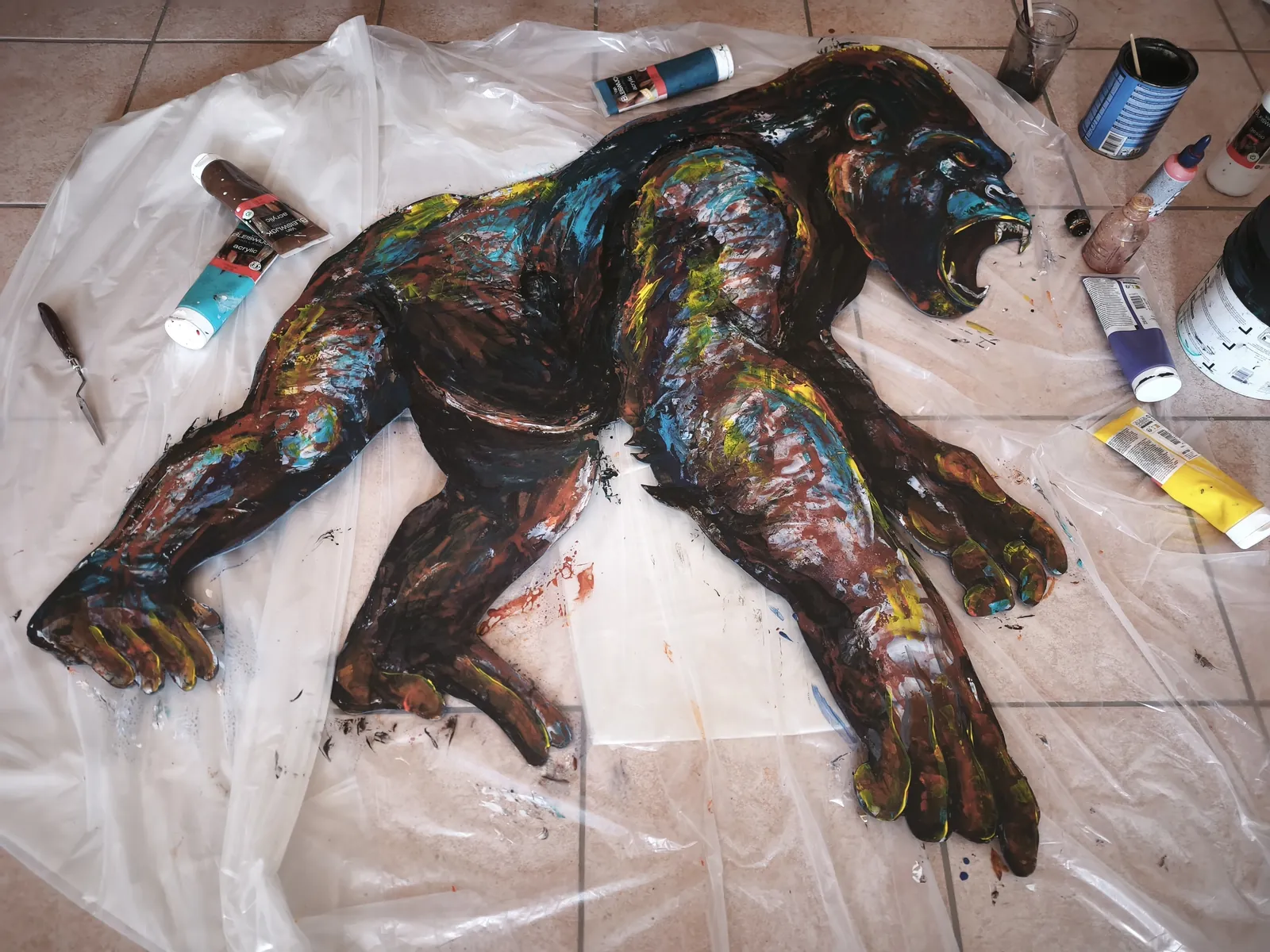 Le Conquérant en cours de réalisation dans l'atelier : panneau Isorel découpé à la silhouette du gorille posé au sol, entouré des tubes d'acrylique et du couteau de Camille